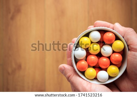 Top view of colorful candies in white bowl on man's hand with copy space. Wooden background. Colorful bubble gums.