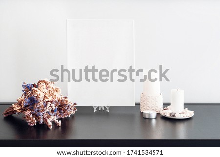 Blank white canvas for artist's mock-up, dry flowers bouquet, candles on black table and white wall. Minimalism style. Mock-up design for artists.
