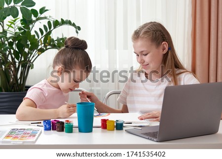 Two happy sisters painting at home, rainbow drawing