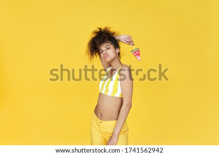 Cool gen z african american pretty gen z teen girl wearing fashion trendy cloth top holding watermelon candy ice cream looking at camera standing isolated on yellow summer studio background. Royalty-Free Stock Photo #1741562942