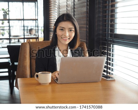 Businesswoman using laptop in coffee shop.Young asian woman in suit sitting and using laptop on wooden table near the window at modern office.