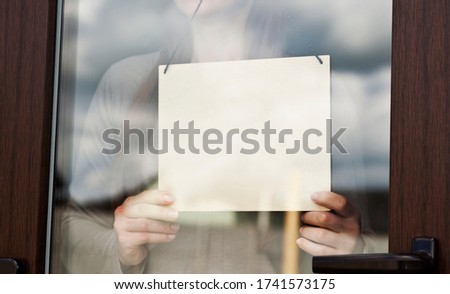 Woman holds the blank wooden sign behind the glass door