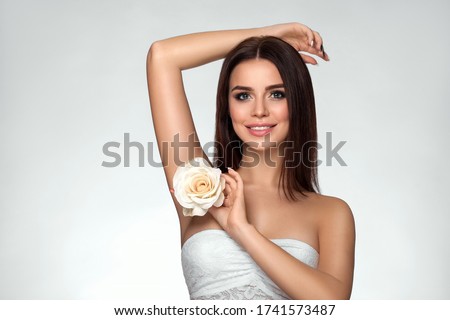 Attractive beautiful young woman with white rose near her face. Spa concept of body skin care. Beauty smiling girl with raised hand up. Armpit and hair removal Royalty-Free Stock Photo #1741573487
