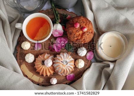 tea with lemon in a cup on a wooden tray, meringues, cookies and a cupcake, flowers, candle, linen cloth background