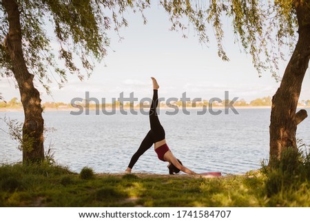 young sport woman practicing yoga outdoors at the lakeshore