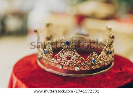 Christian golden crown for holy matrimony on red table in church. Wedding spiritual ceremony. Golden crown with red and blue stones close up. Orthodox wedding tradition