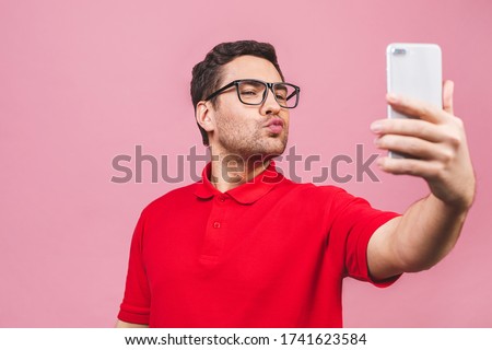 Close up portrait of a cheerful young bearded man taking selfie over pink background. 