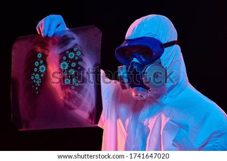 COVID-19 or 2019-nCoV. Portrait of a doctor in a protective PPE suit showing an x-ray picture of the lungs of a patient with coronavirus pneumonia.  Royalty-Free Stock Photo #1741647020