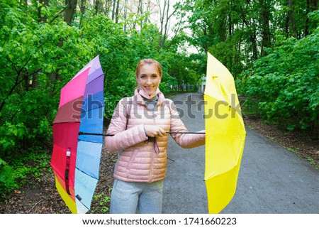 Young woman in a medical mask with colored umbrellas walks in the forest during quarantine