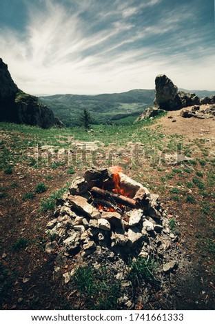 Vertical photo of campfire in the top of hill with perfect view. Bonfire in forest on sunnyday with view on  cloudy sky and mountains.
