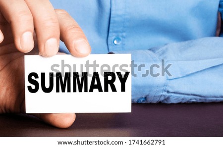 A man holds a business card with the written word SUMMARY