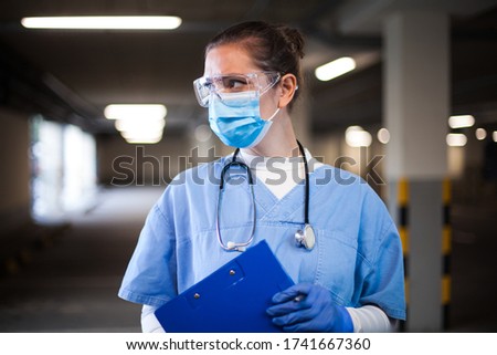Female ICU doctor in hospital parking lot,first responder frontline key medical worker,holding clipboard patient medical card,looking away,emergency service during COVID-19 coronavirus pandemic crisis Royalty-Free Stock Photo #1741667360