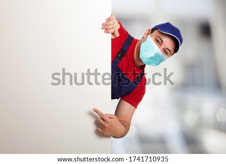 Portrait of a friendly masked worker pointing his finger to a blank board