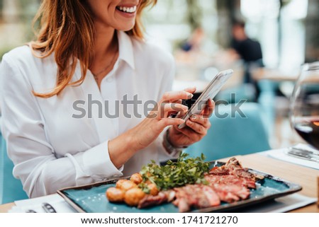 Young beautiful woman enjoying in tasty and nicely decorated meal. She sitting in expensive restaurant and using her smart phone for food photography.