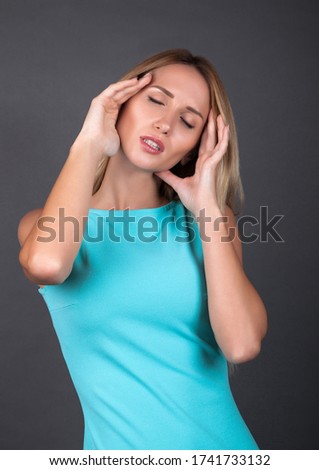 Portrait  of an attractive blond woman standing  in blue dress and suffering from a headache. Stock Photo