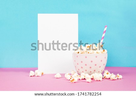 Fresh popcorn in a white pink bowl on pink and blue background with the blank paper page