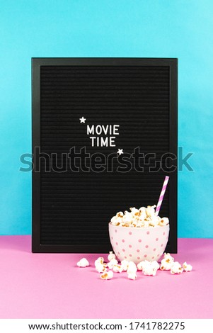 Fresh popcorn in a white pink bowl on pink background with the board ''Movie Time''