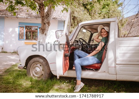 A beautiful attractive caucasian woman with a straw hat is sitting in a white old truck in the countryside