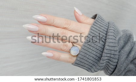 Female hand with long nails white manicure and a bottle of nail polish