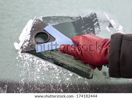 Picture of a hand holding window scraper and removing ice of the car window