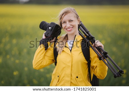 Happy woman holding digital camera and tripod outdoors