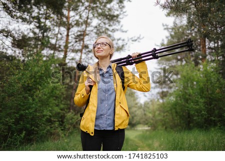 Woman walking among forest with tripod, camera and backpack
