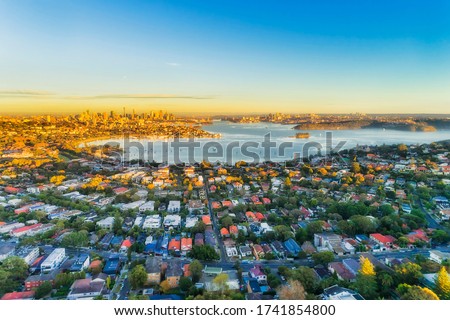 Wealthy Eastern suburbs of Sydney city around Harbour in aerial view with soft morning light and blue sky.