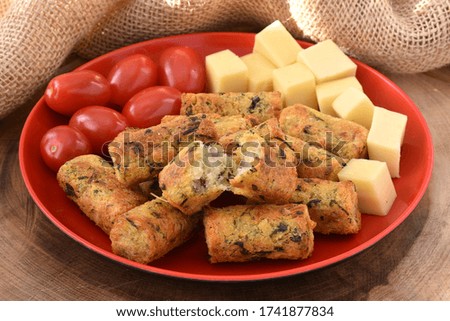 A portion of cod fish croquette with cherry tomatos and cheese in a red plate on a wooden board and a rustic fabric at the background
