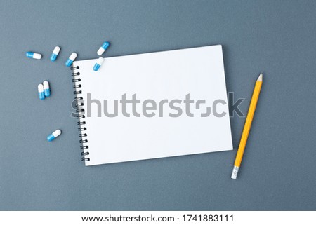 Open notebook with clear page with yellow pencil and capsule pills on grey background. Design business, medicine supplies or medical concept. Ready for adding or mock up. Top view.