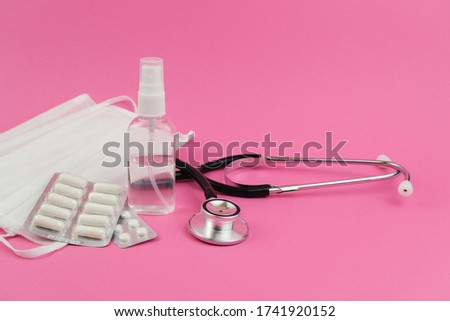 White heart, medical stethoscope, pills, masks and antiseptic on pink background.