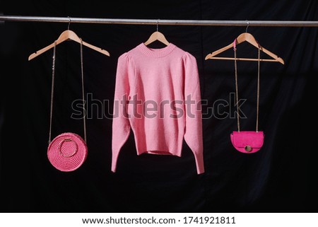pink sweaters with pink handbag with round pink rattan handbag on hangers –black background 
