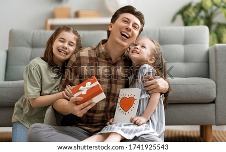 Happy father's day! Children daughters congratulating dad and giving him postcard. Daddy and girls smiling and hugging. Family holiday and togetherness.