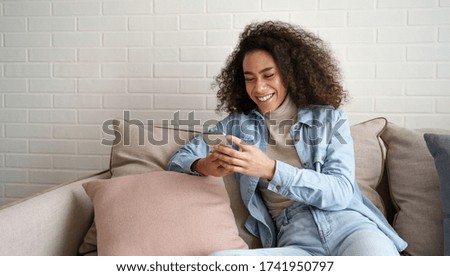 Happy african millennial woman holding smart phone watching social media video content. Smiling young black teen gen z girl using funny mobile app laughing, playing game, chatting on cell at home. Royalty-Free Stock Photo #1741950797