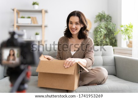 Young confident woman is talking on digital camera recording vlog sitting on sofa at home.