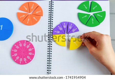 Kids hand moves colorful math fractions on gray wooden background or table. Interesting creative funny math for kids. Education, back to school concept. Geometry and mathematics materials.
