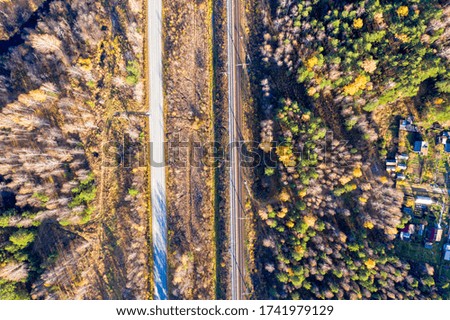 The road runs parallel to the railway. Holiday villages. Flying over the autumn mixed forest during sunset. Ural, Russia. View from above. Overhead shot.