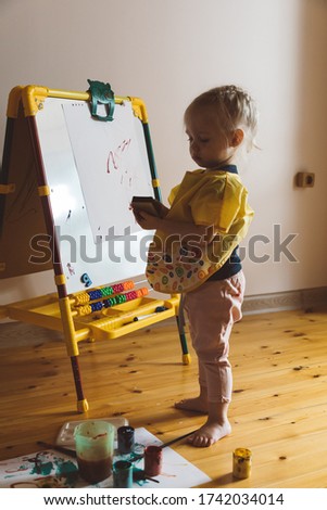 Little girl sits on the floor and draws on an easel