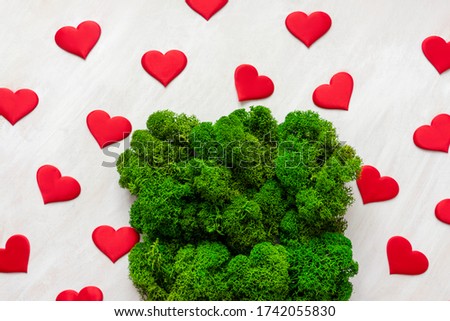 Natural moss texture with red hearts on white wooden background. Top view, copy space.