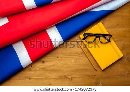 Top view of the flag of Great Britain lies on a wooden table next to an open notebook with a pencil. The concept of teaching English and studying at an English university. Advertising space