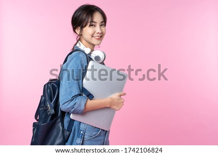 Portrait of smiling young Asian college student with laptop and backpack isolated over pink background