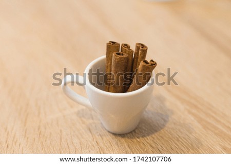 Cup with aromatic cinnamon sticks on wooden table, close-up.
