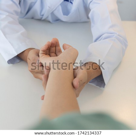 Asian orthopaedic doctor doing physical examination in the patient with wrist pain and numbness at the clinic. Selective focus at right hand. Medical concept.