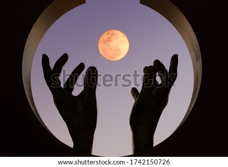 Figures of hands moving the fingers trying to cover the moon at sunset