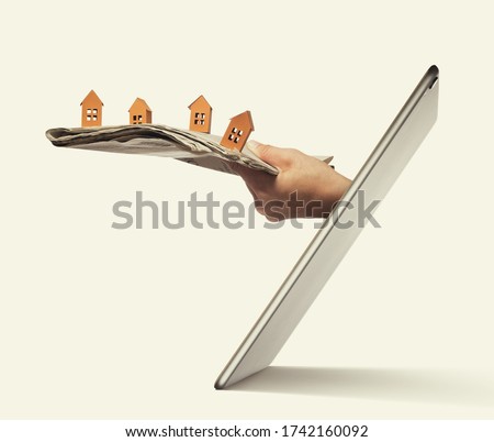 Newspaper with paper houses stick out of a tablet pc screen. Buying a house via internet. Concept of modern technologies in real estate industry. 