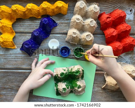 Children's hands paint the egg box with different colors