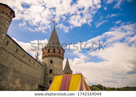 medieval stone castle wall and tower heritage landmark site of historical festival event with tent of camp place, perspective photography blue sky white clouds background scenic view 