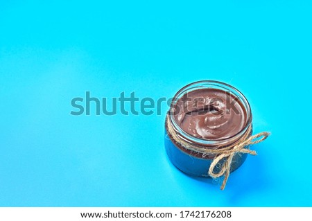 Single glass transparent jar with rope full of melted chocolate or cream lies on blue desk on kitchen. Concept of nutritious breakfast or lunch. Space for text