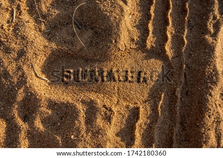 Summer sand. Picture of word "summer" in the sand at the beach inside of a footprint. Photo with textures. Seasonal theme summer. Editing space. Soft light at sunset time.