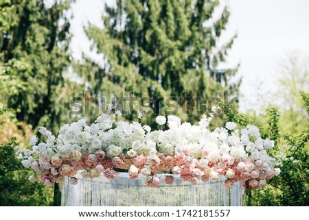 Very beautiful outside ceremony. classical wedding in forest. The arch is wooden. White flowers. Brown chairs. Rite. Bride and groom. Decor. Floristics. In the open air. Path from the petals of roses.