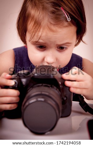 Humorous portrait of little cute child girl photographer with DSLR camera. 